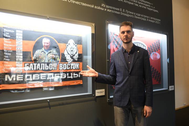 Никита Аникин показывает один из экспонатов выставки — знамя легендарного взвода «медведевцев» батальона ополчения Донбасса «Восток» с автографами участников боя за высоту Саур-Могила